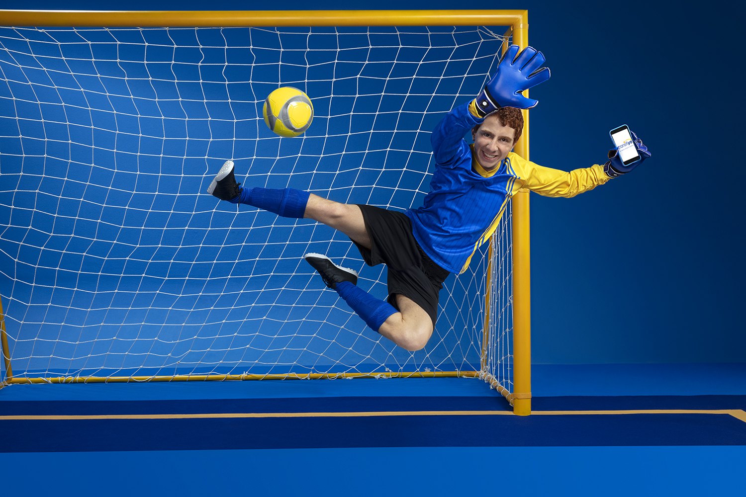 A goalkeeper in yellow flying across the goalmouth against a solid blue field