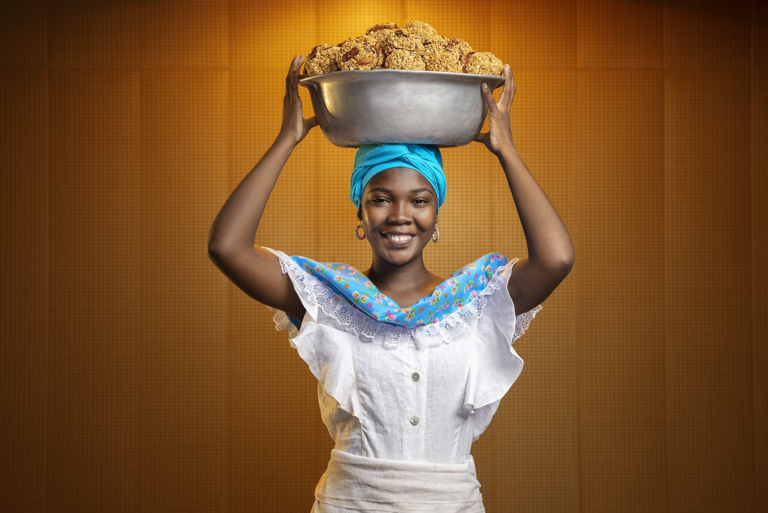 A palenquera in white holds a bowl of fruit on her head