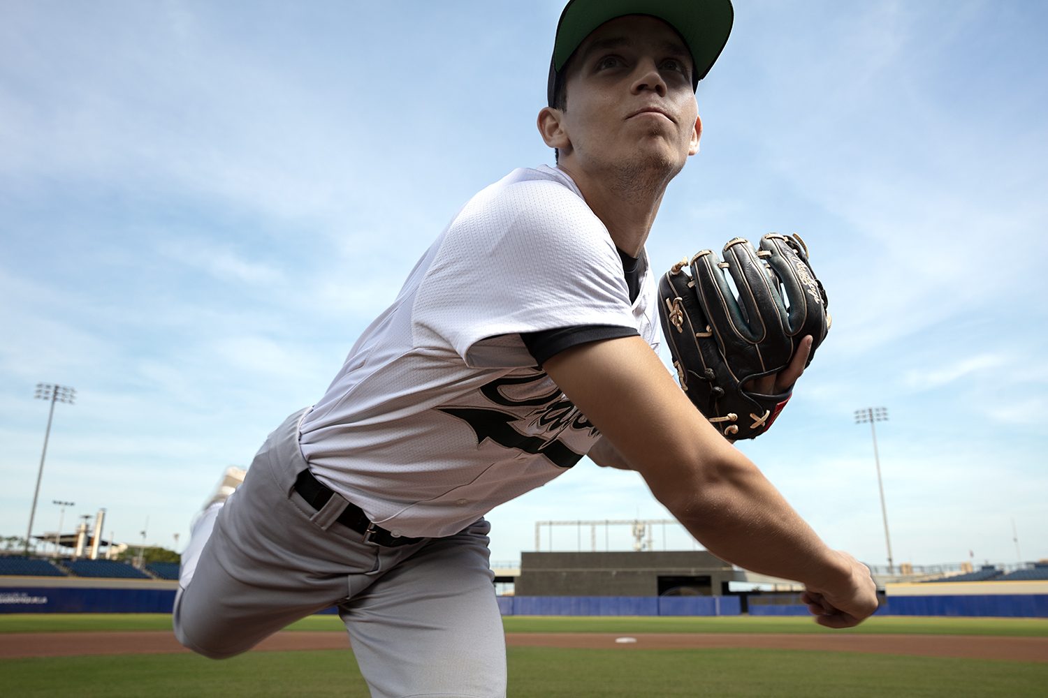 A baseball pitcher winds up under a bright sky
