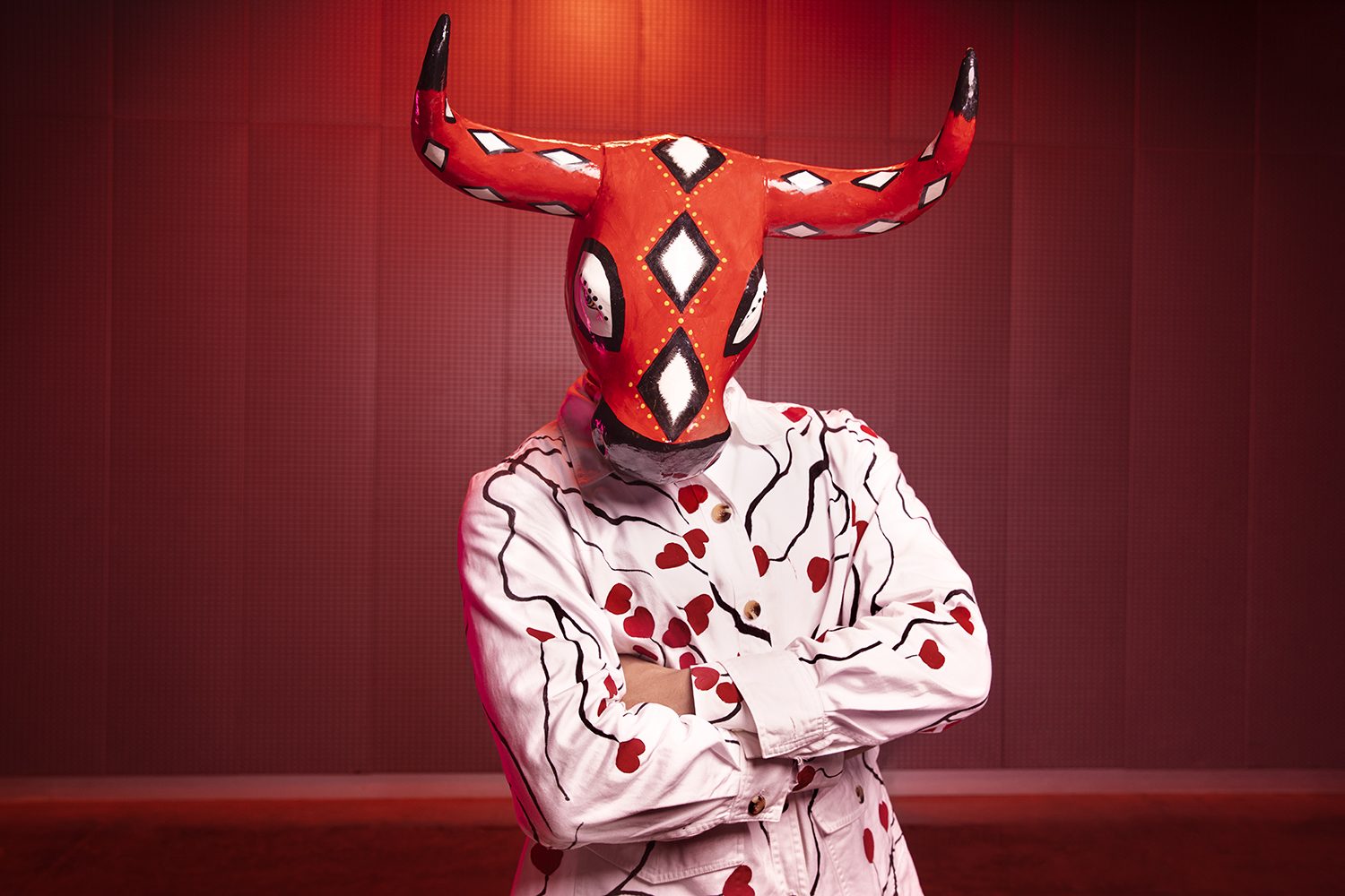 A carnival devil in a red horned mask against red
