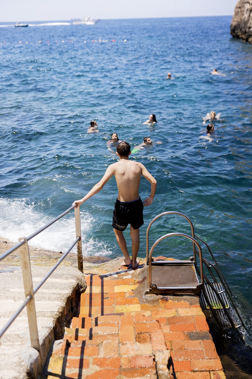 A swimmer steps off the rocks into clear blue water