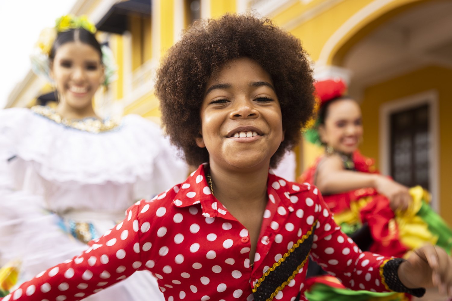 A boy in red polka dots dancing with performers behind him