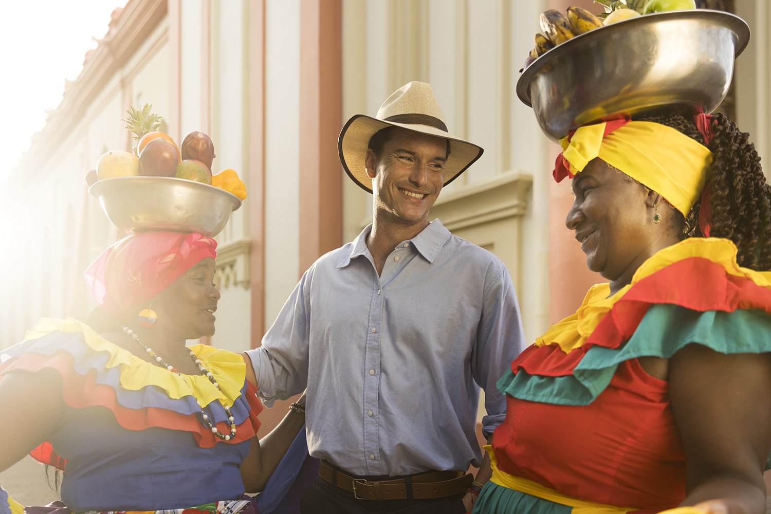 A man in a straw hat between two fruit sellers on a colonial street