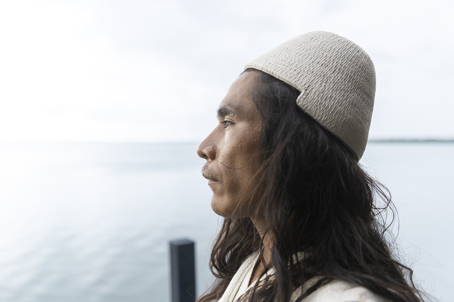 A woman in a knitted cap in profile against flat pale water