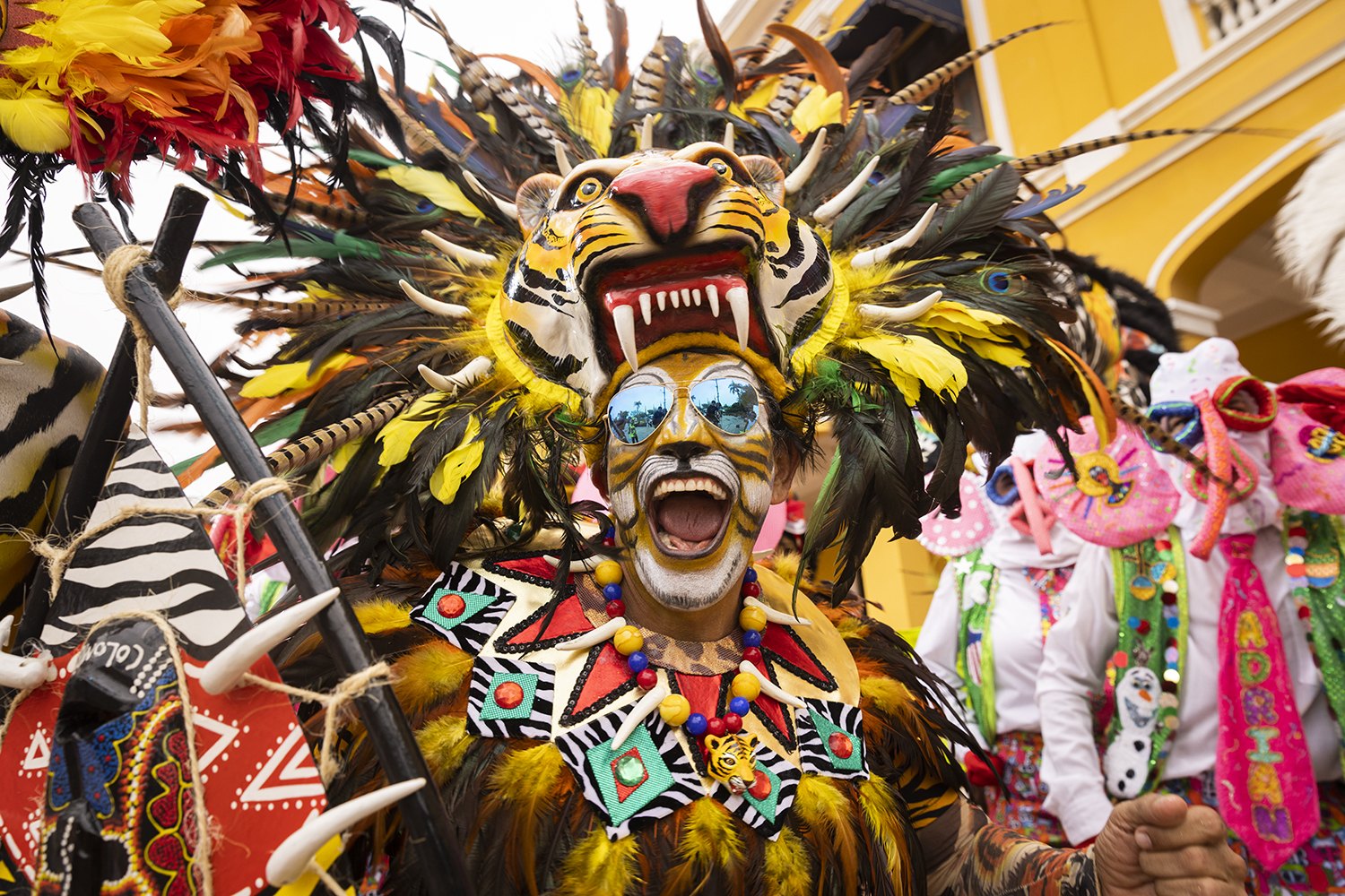 A dancer in a horned carnival headdress mid-roar in the street
