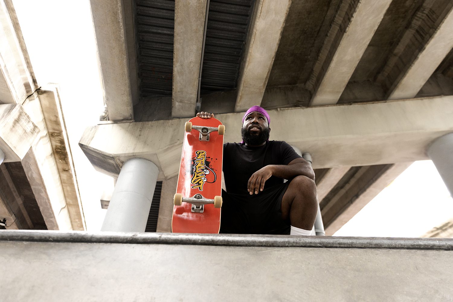 A skater sits in the shade with his board under the overpass
