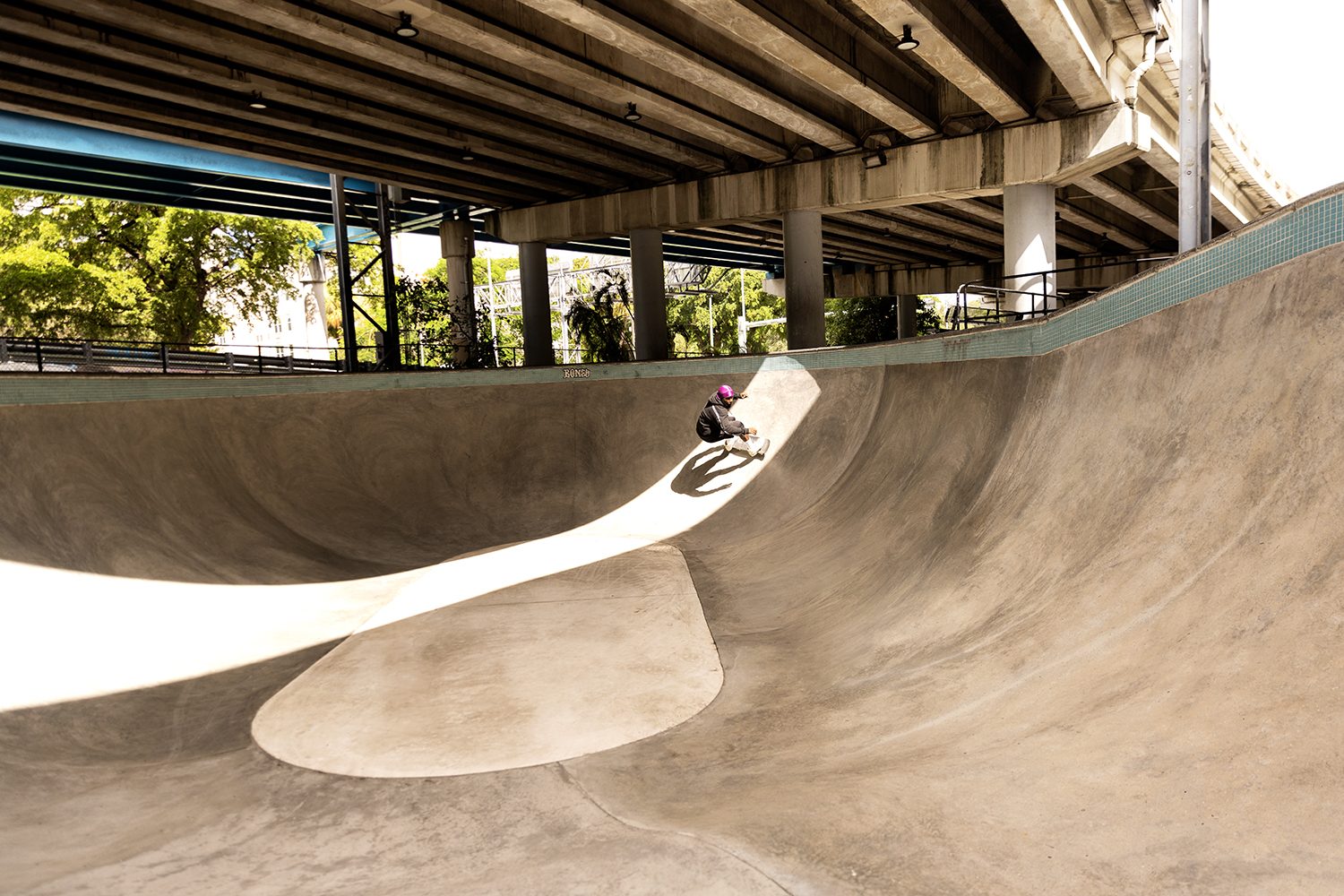A skater carves a concrete bowl in the shade
