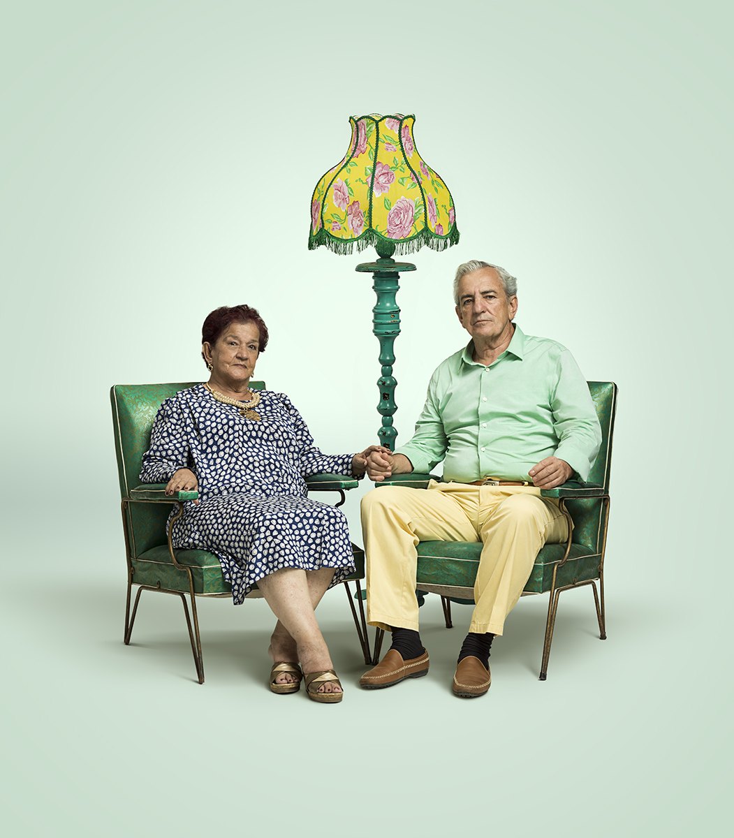 An elderly couple seated in their own armchairs beside a fringed standard lamp
