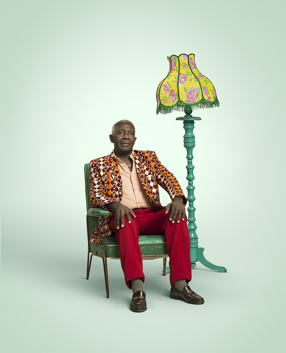 A man in red trousers and green shoes sprawled in an armchair under the same lamp