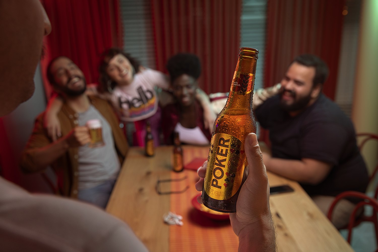 A bottle held up in the foreground with the table of laughing friends thrown out of focus behind it