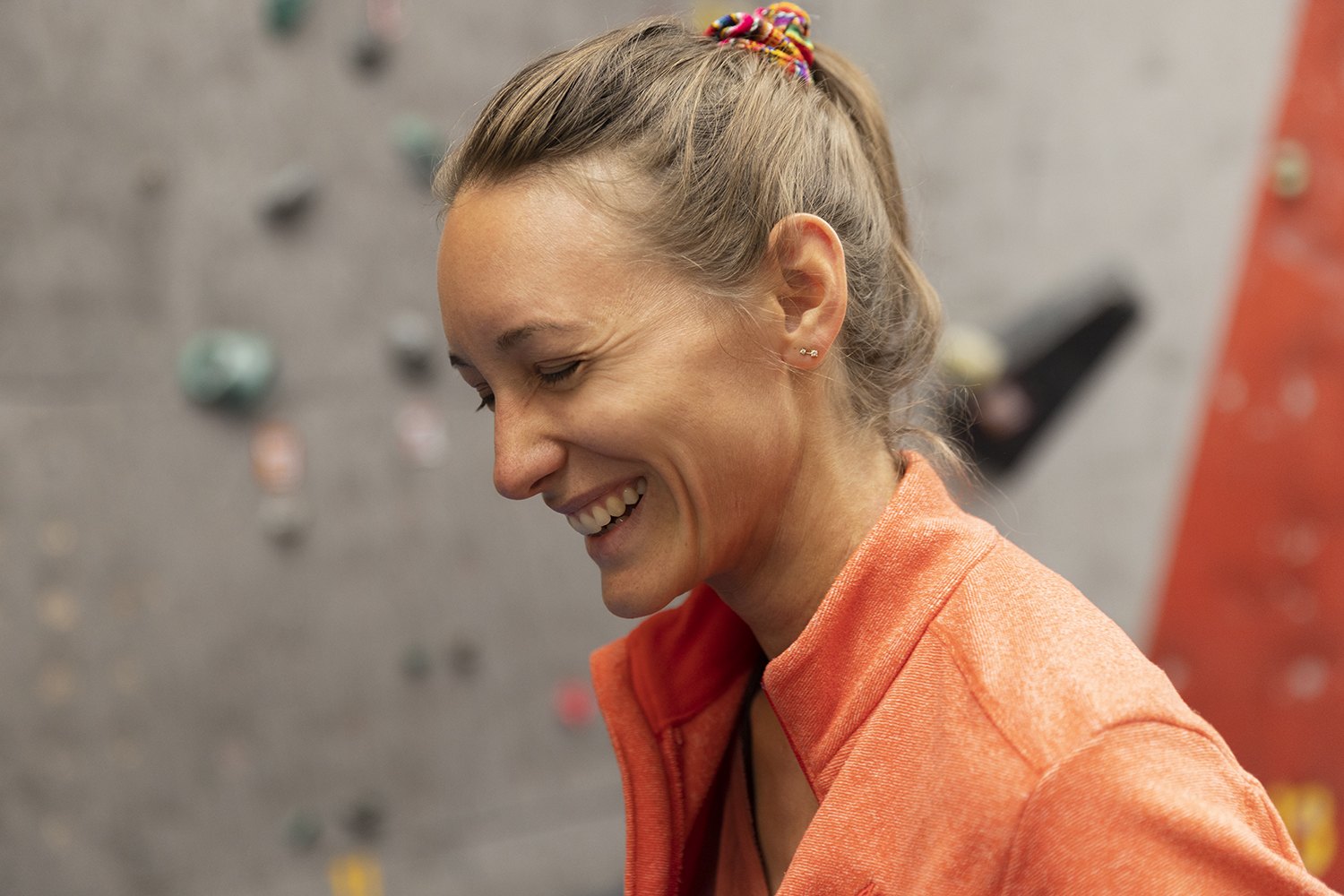 Laughing with her hair tied back, grey wall filling the frame