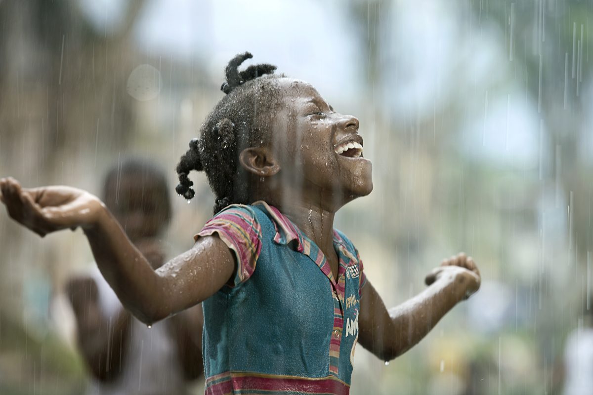 A child laughs with arms outstretched in the falling rain in Lloró, Chocó