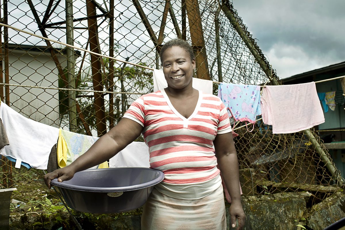 A woman gathers rainwater run-off in a metal basin