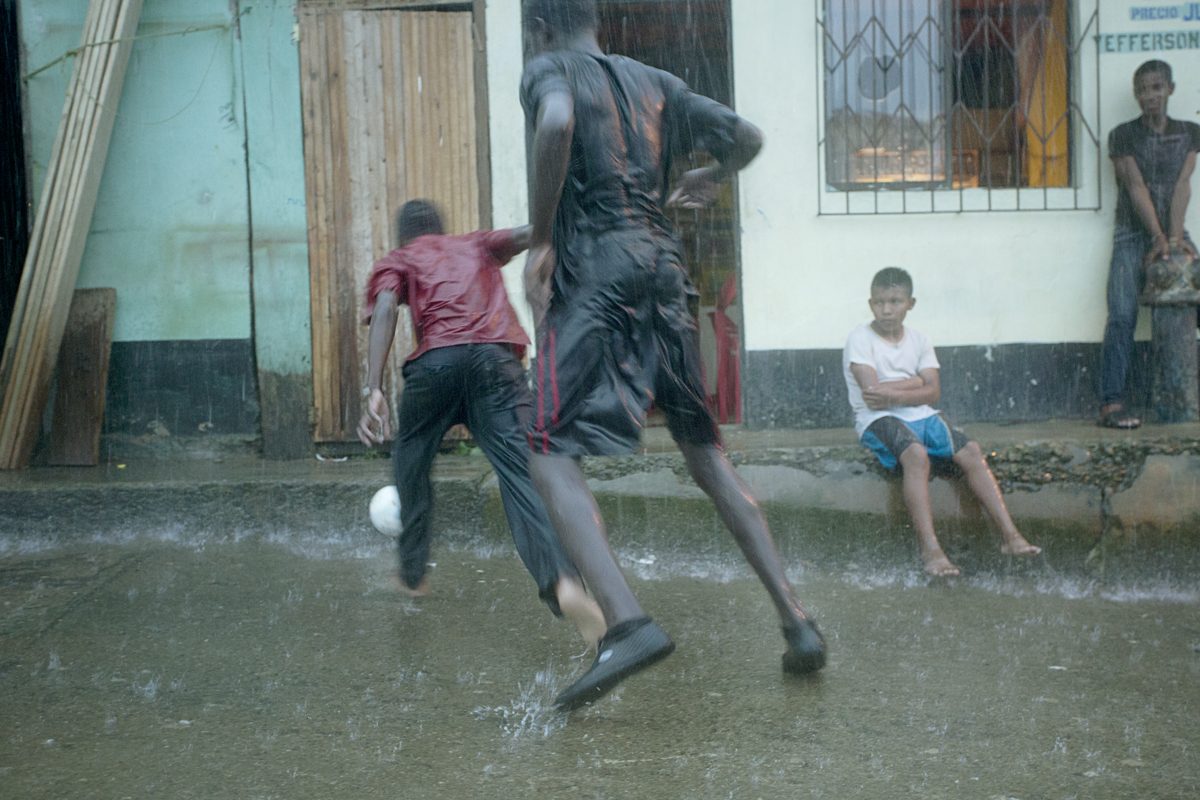 Children run and play through a downpour on a village street