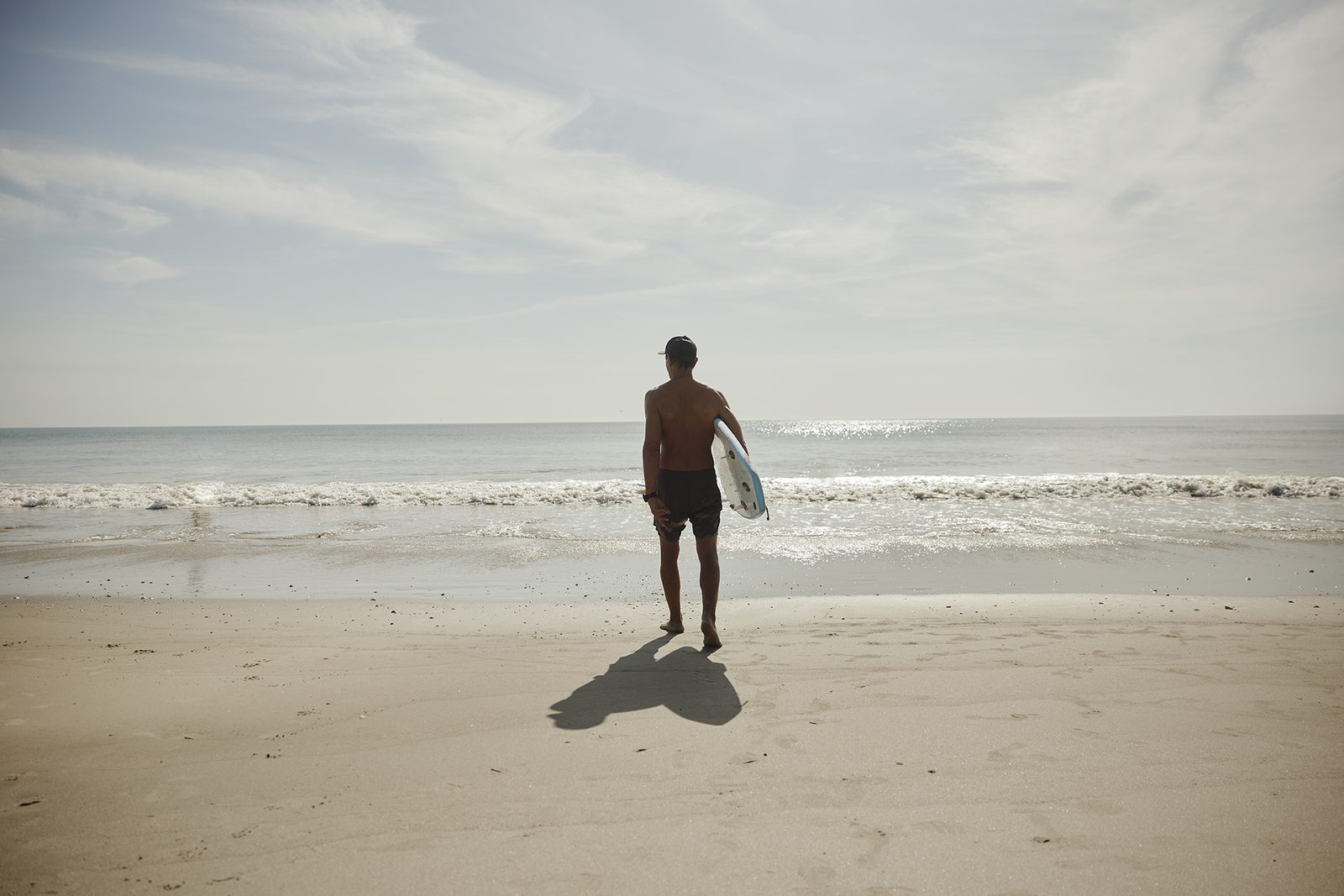 A lone surfer walks toward the sea, board under arm