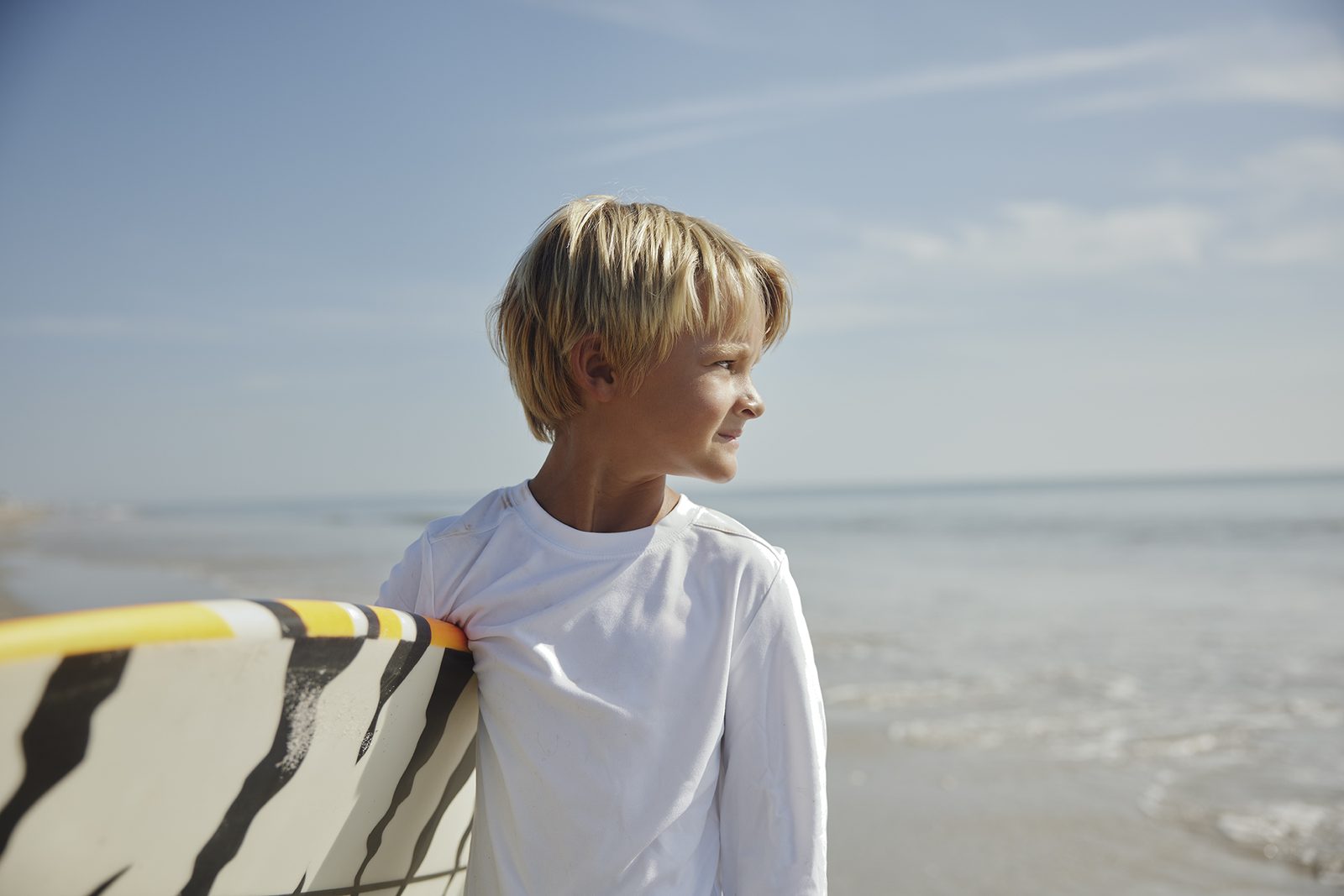 A boy in a rash guard holds a striped surfboard