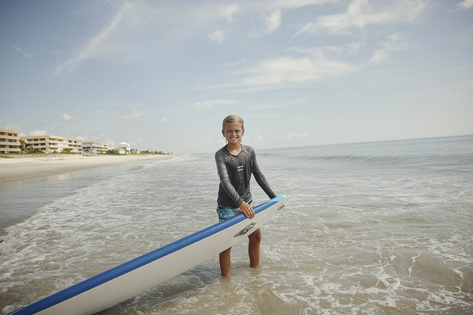 A young surfer wades in with a board at the shoreline