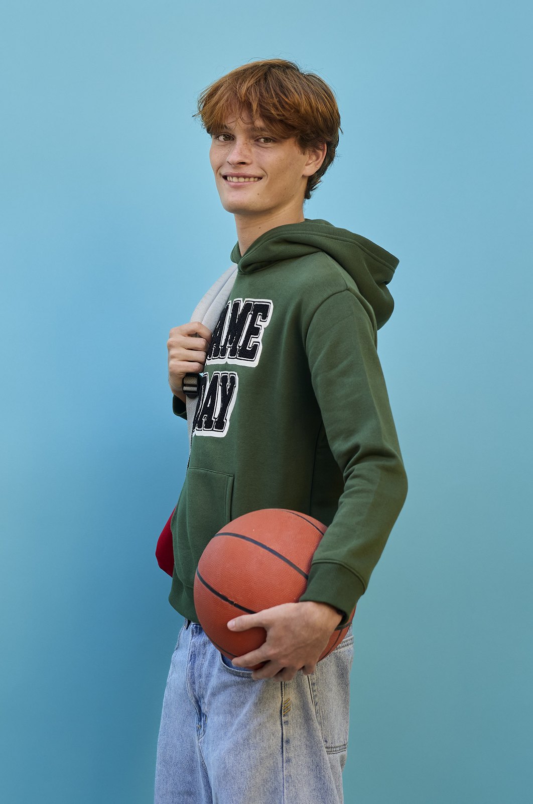 A student in an olive hoodie holding a basketball under one arm
