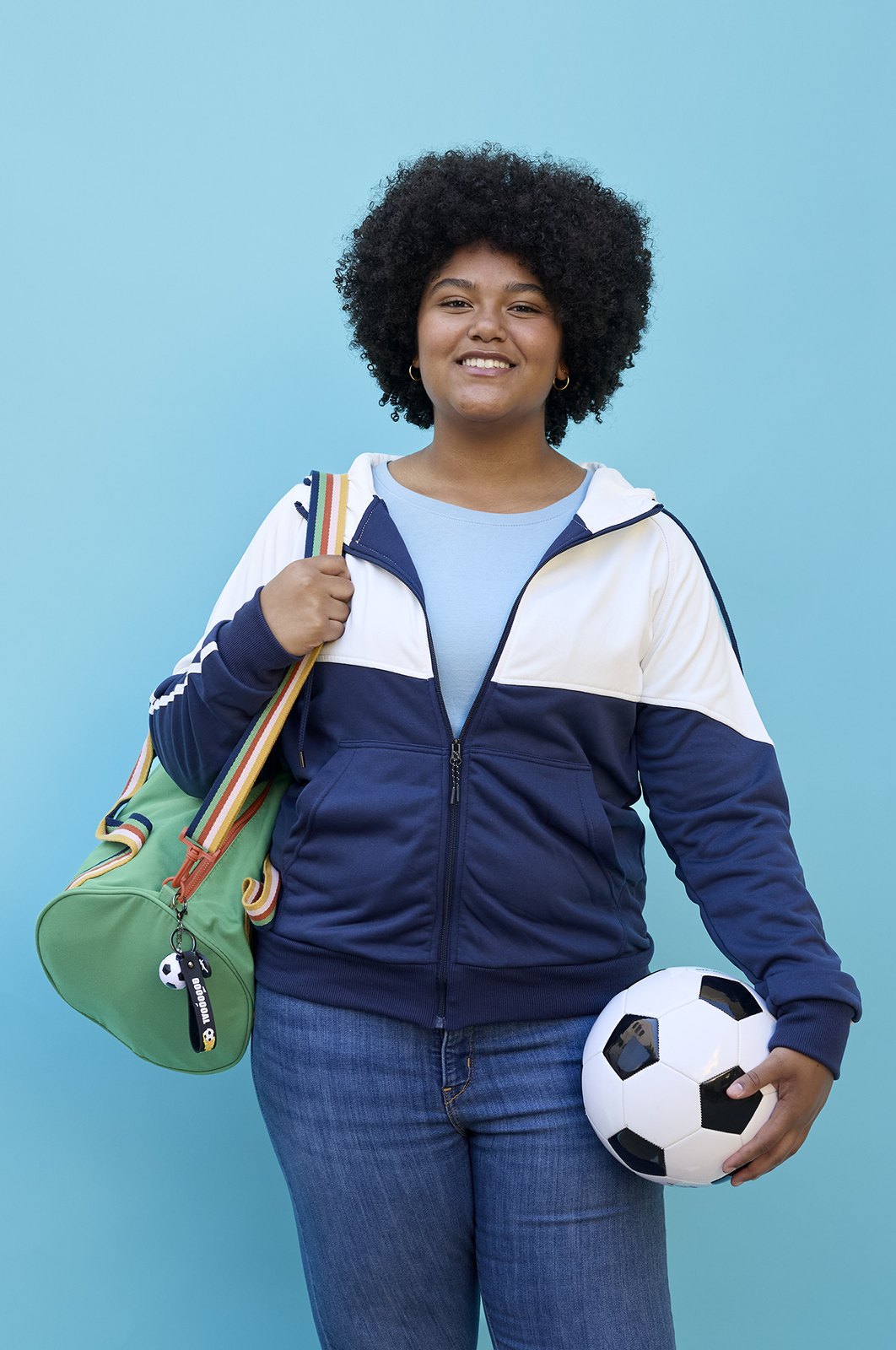 A student with a duffel bag over the shoulder and a football held at the hip