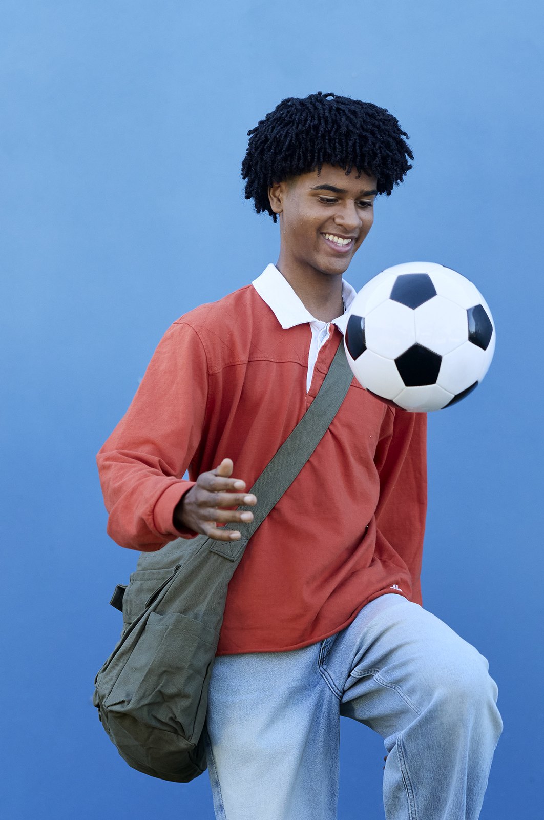 A football caught mid-air beside a student in a red rugby shirt on a blue backdrop