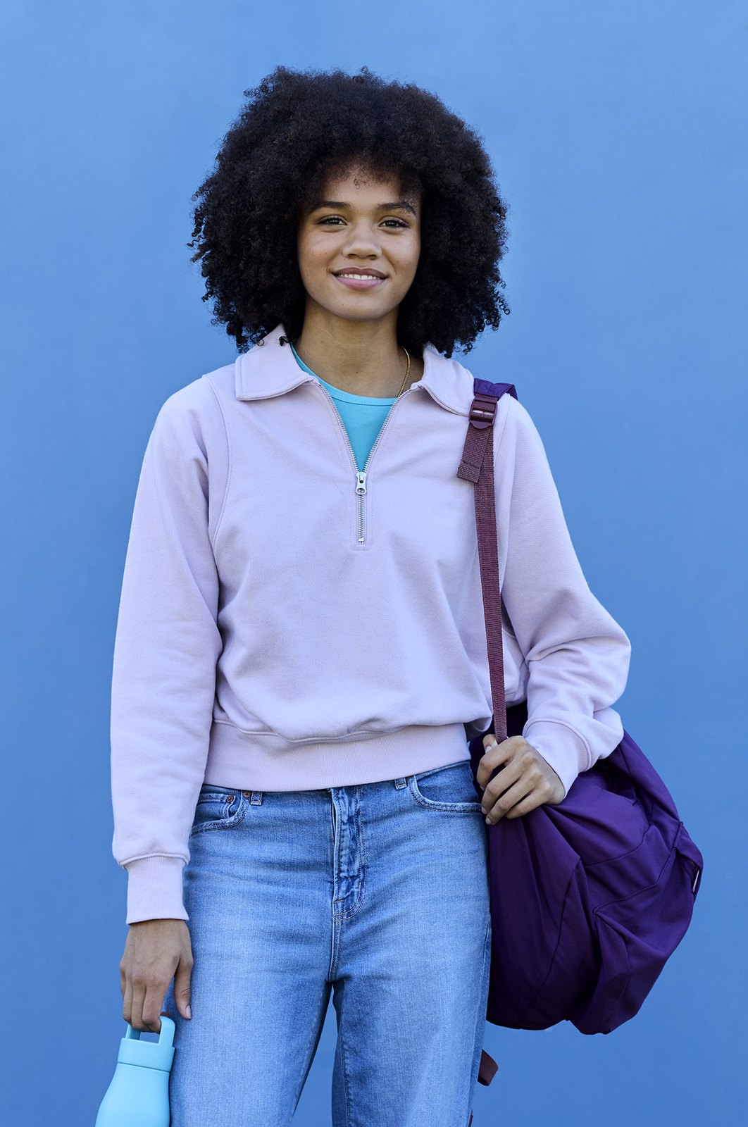 A student in a striped tee with blue headphones on, bag strap crossing the chest