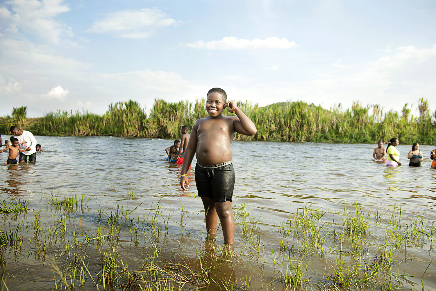 A boy grins in the shallows of a river wetland outside the city