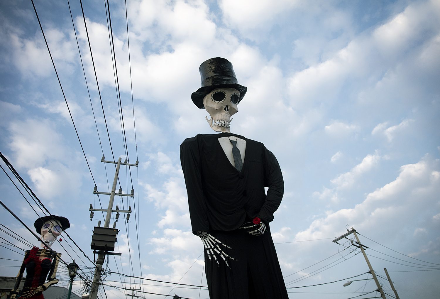 A giant skeleton figure stands against the sky during Día de los Muertos