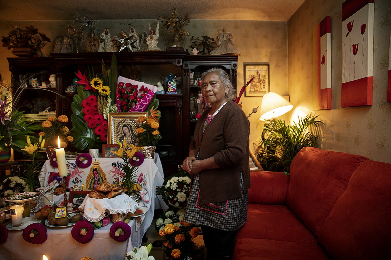 A man stands beside a family altar decorated with marigolds and candles