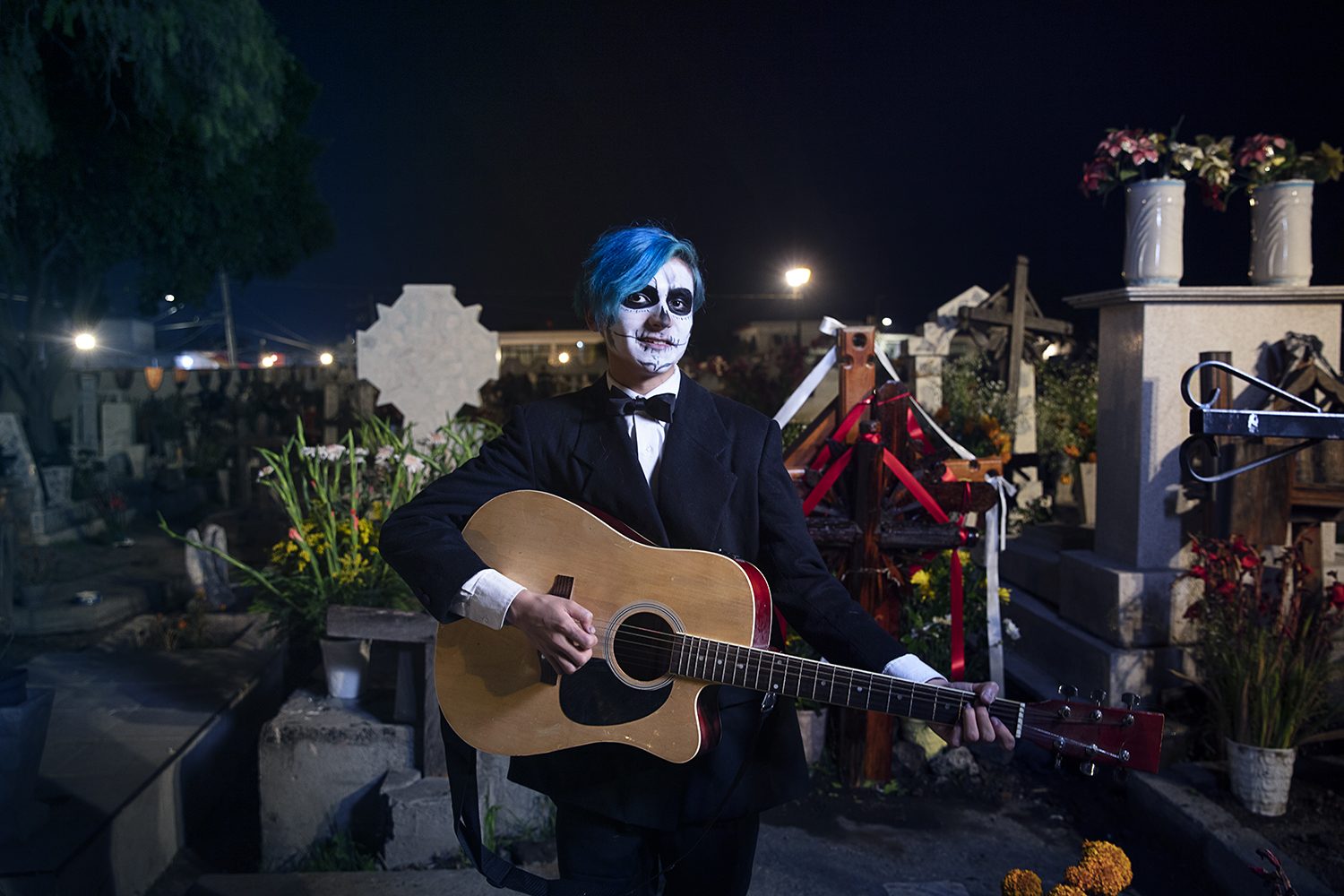A musician with a guitar in a candlelit cemetery at night