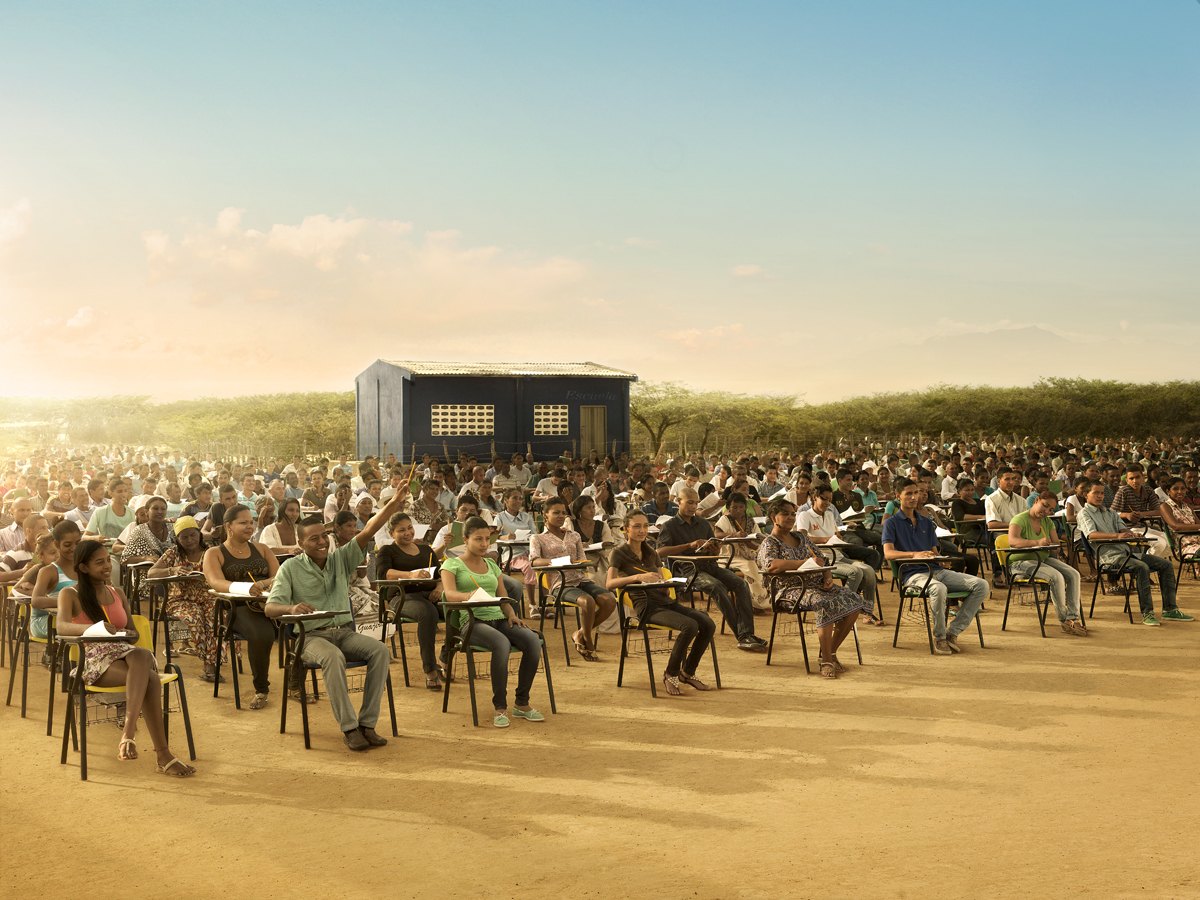 Hundreds of workers seated in rows across open arid ground at first light