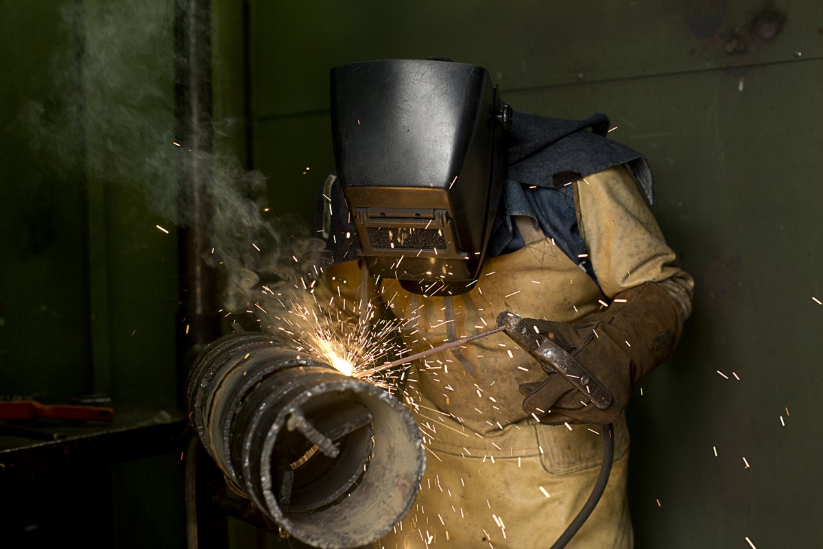A welder mid-cut, sparks thrown out across the frame