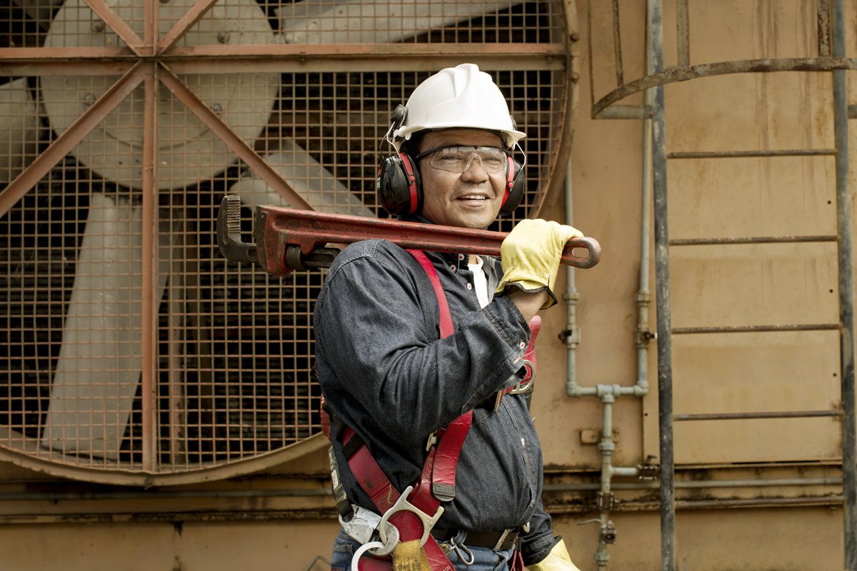 A worker in harness and hard hat carrying pipe along a gantry