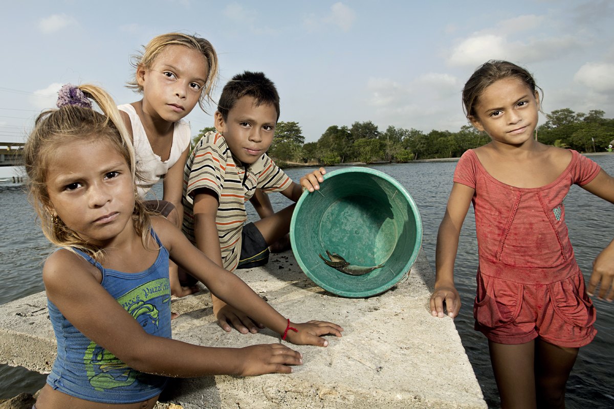 Children crouched at the water edge playing with a plastic bowl