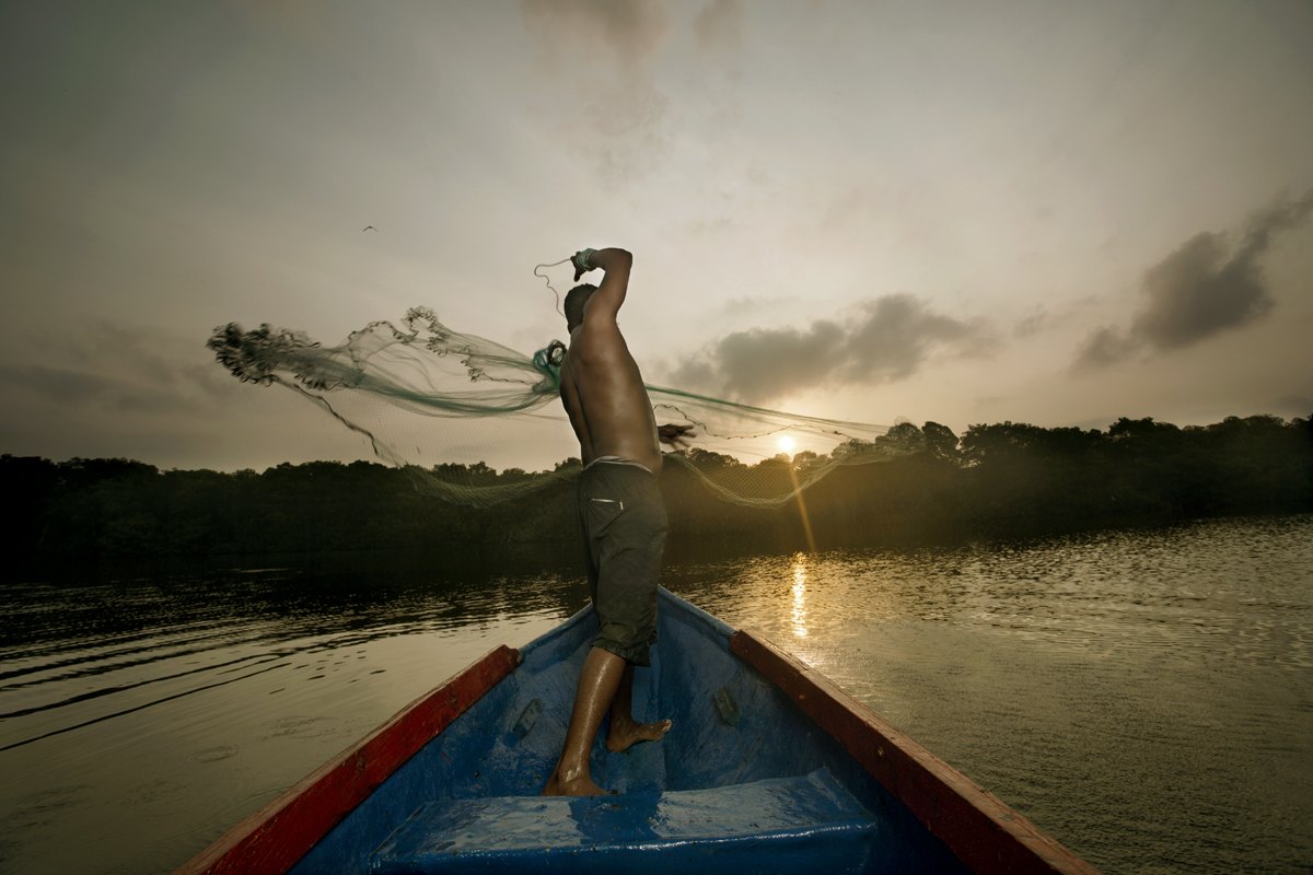 A fisherman casts his net from a canoe as the sun comes up over the water