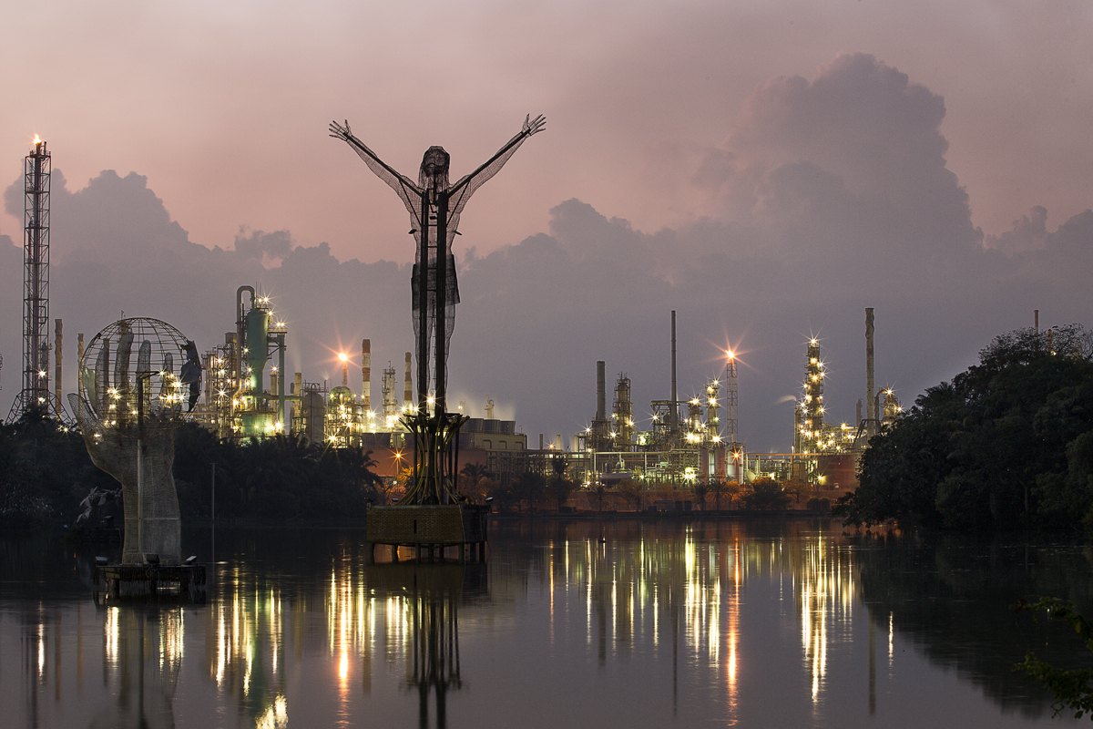 The refinery burning bright at night, its lights doubled in the river