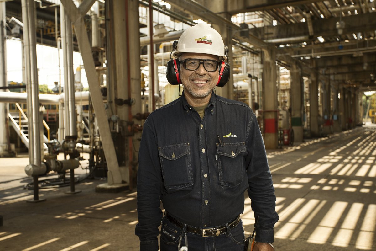 A worker in a white hard hat framed by pipework inside the plant