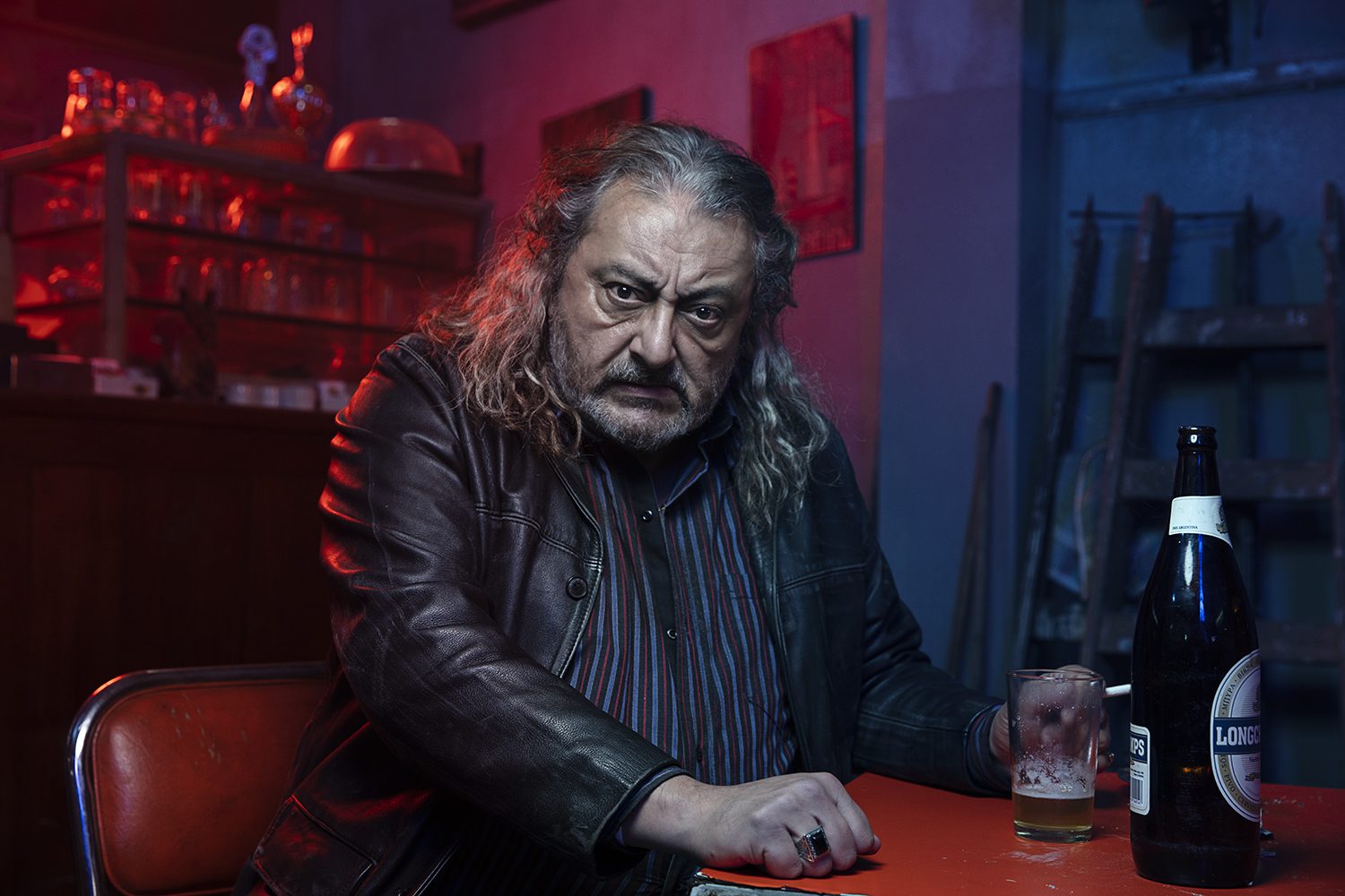 An older character lit in red at a bar