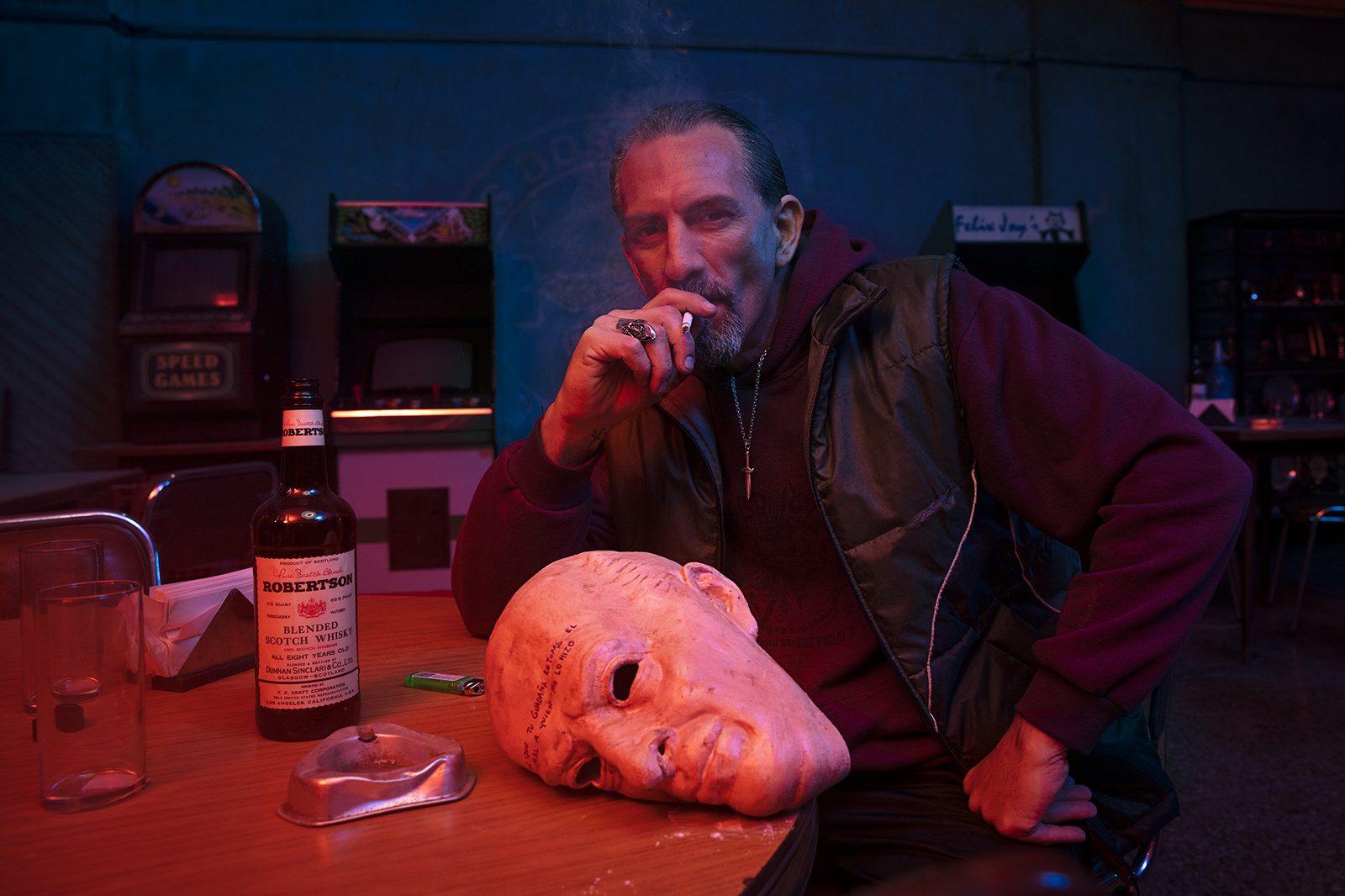 A character seated at a table in moody lighting