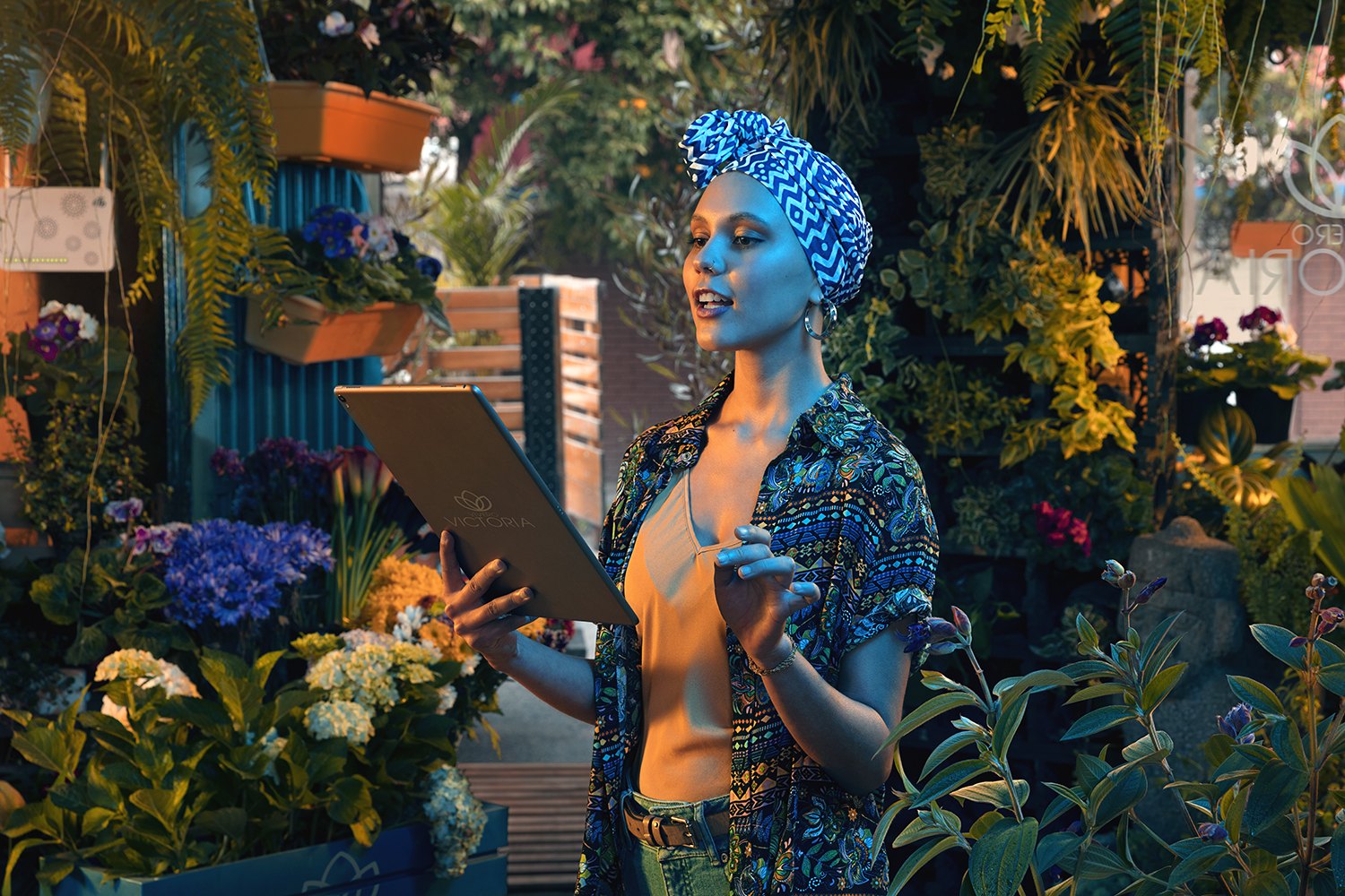 A woman with a tablet standing among dense houseplants in blue and amber light