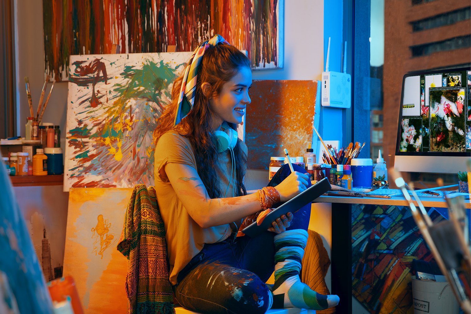 A painter in headphones at her easel, canvases and colour all around