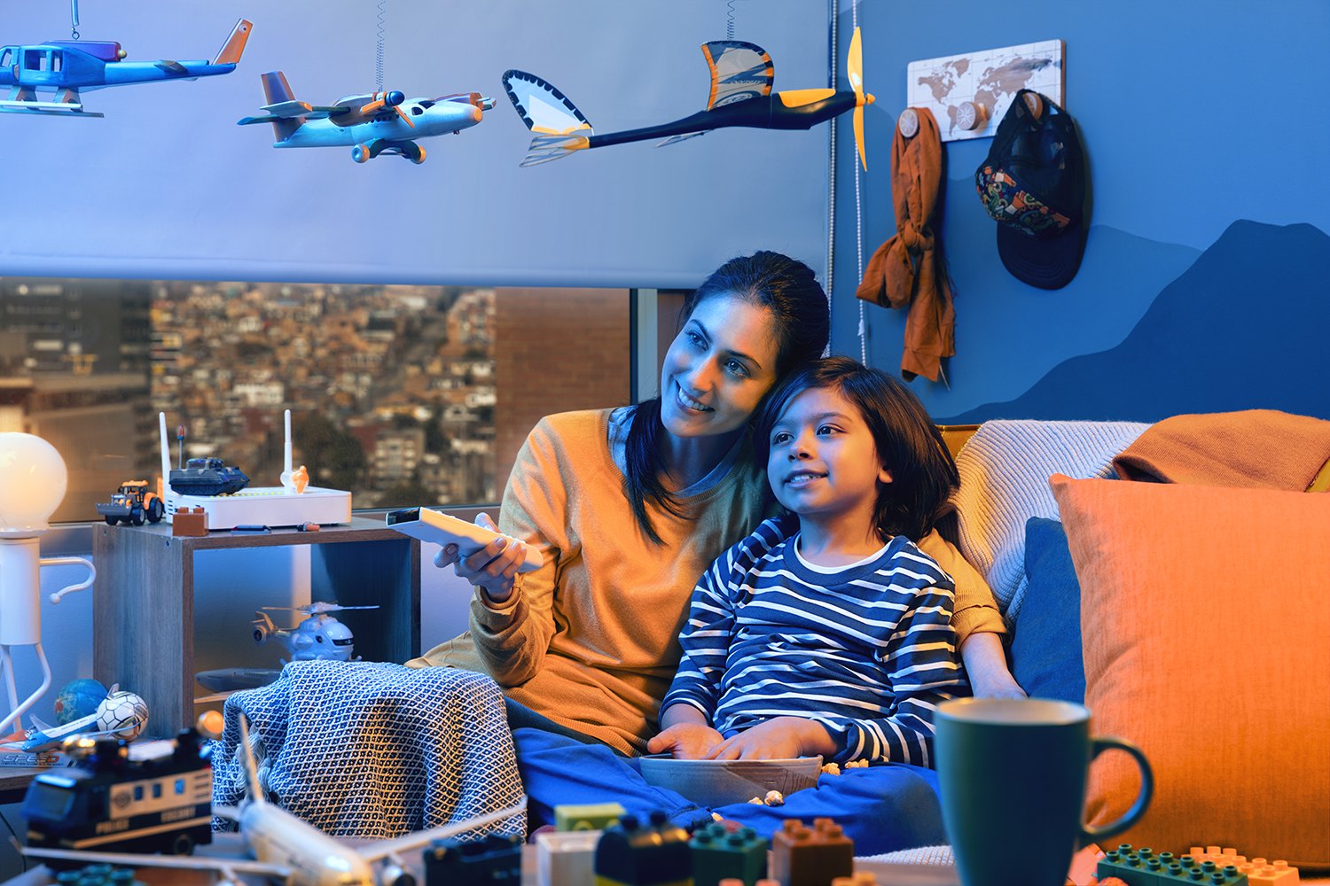 A father and daughter on the sofa, model planes hanging above and mountains through the glass