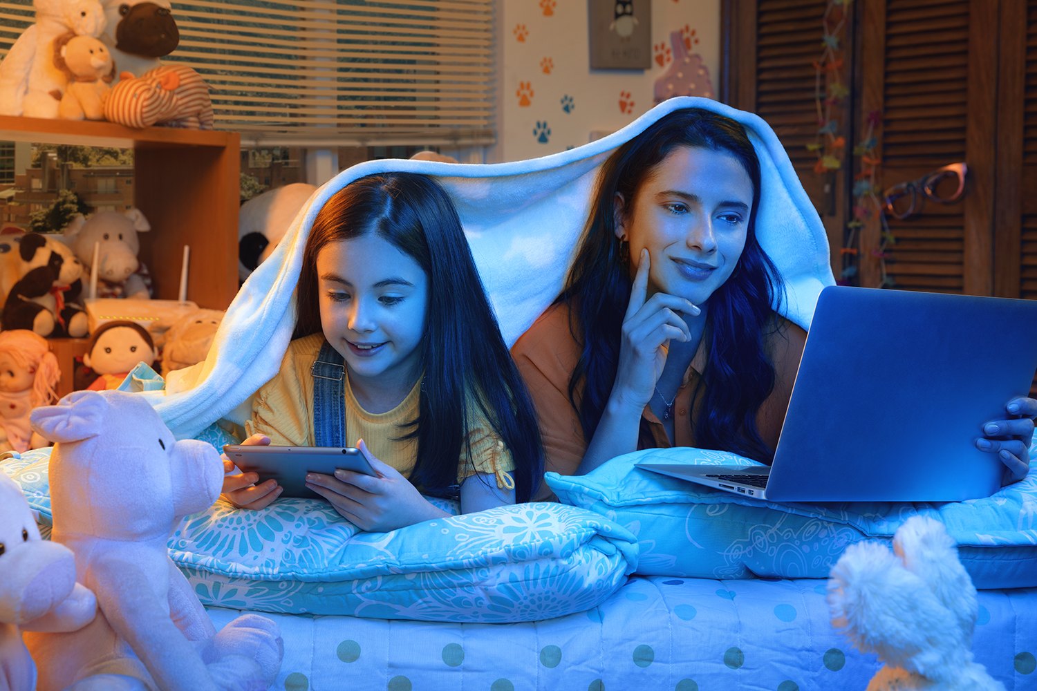 Two girls under a blanket lit only by the screen of a laptop