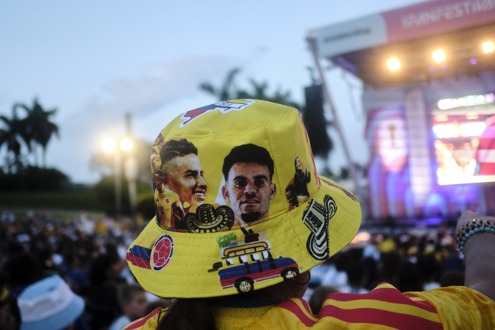 A yellow Colombia bucket hat painted with players and a chiva bus, stage lights beyond