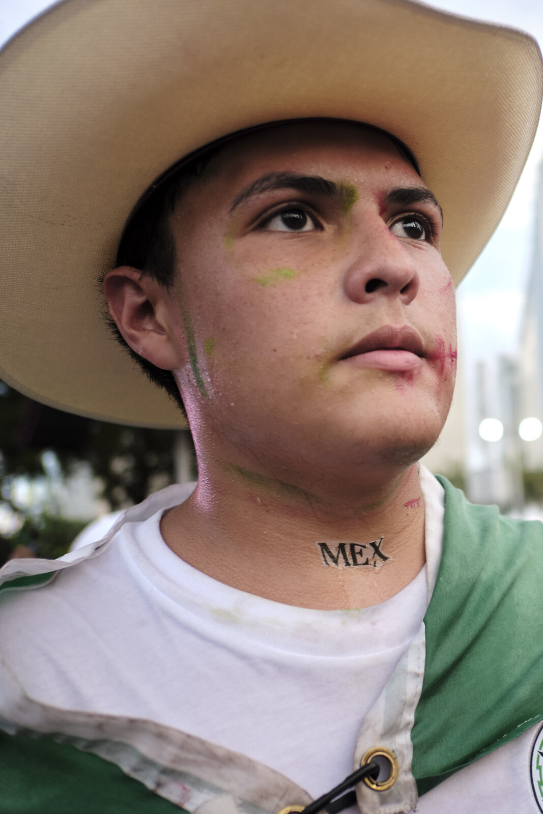 A Mexico supporter in a cowboy hat, flag painted on his cheek, eyes on the match
