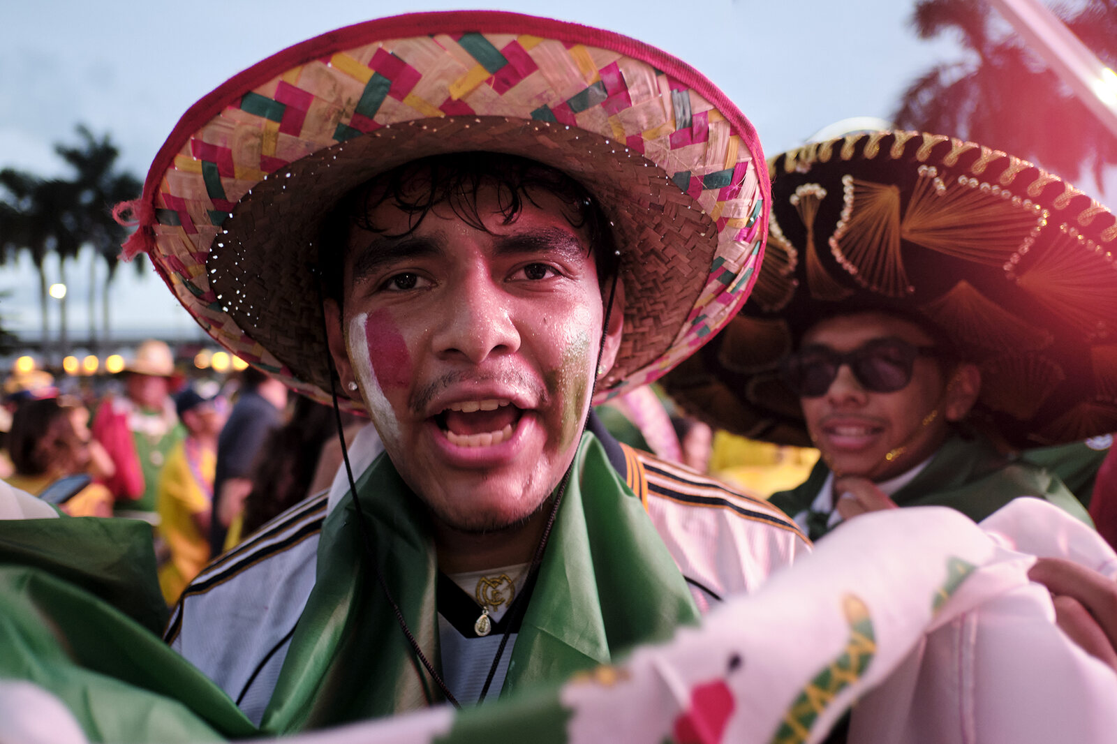 A fan in an embroidered sombrero, wrapped in the Mexican flag, calls out to the crowd
