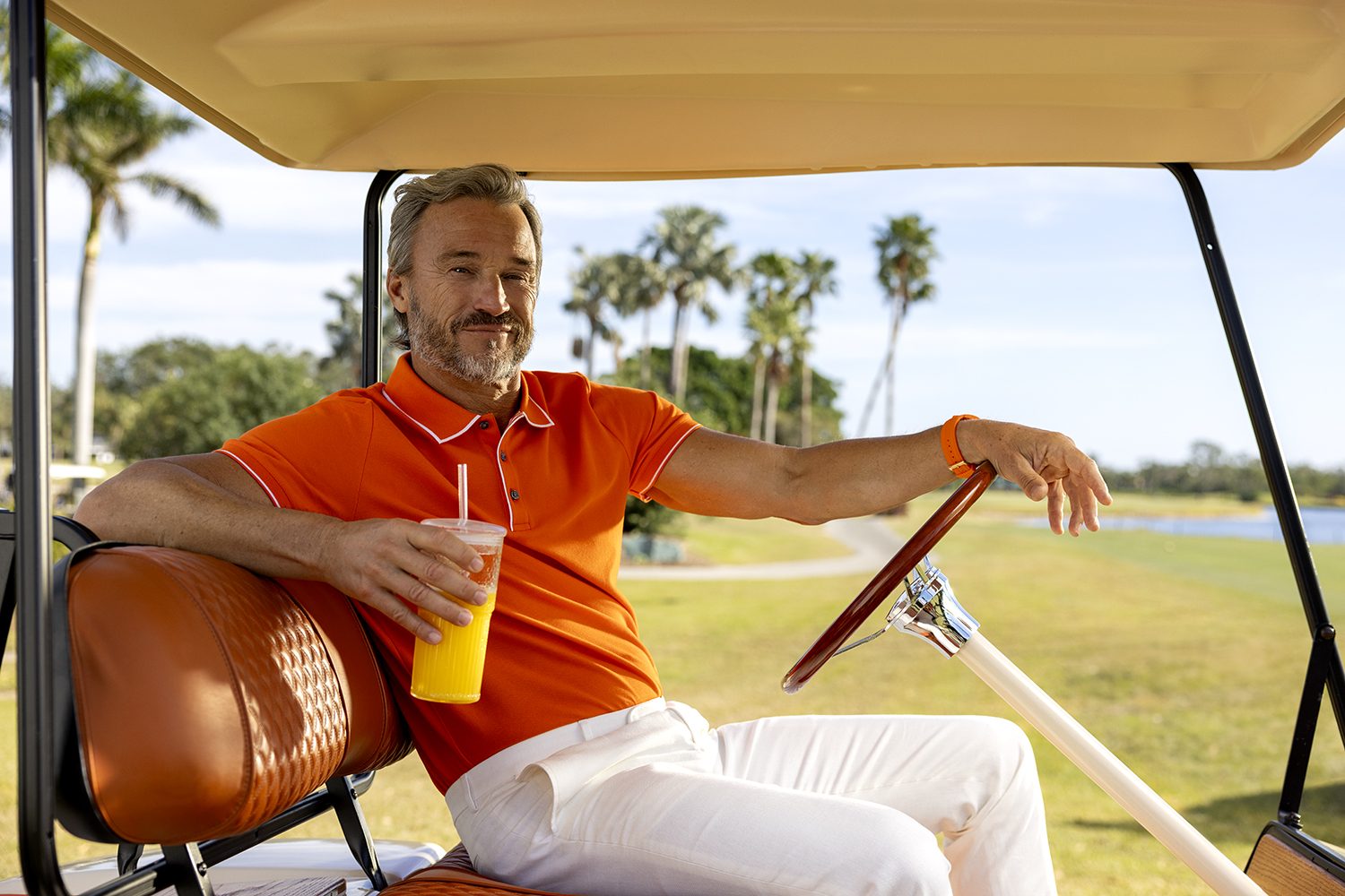 A man relaxes in a golf cart with a glass of orange juice