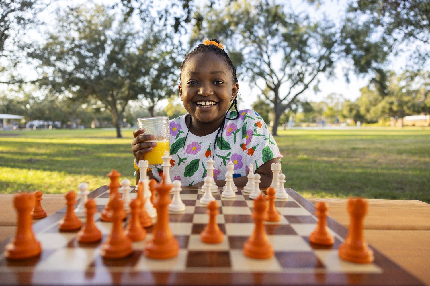 A girl smiles over a chessboard with a glass of orange juice