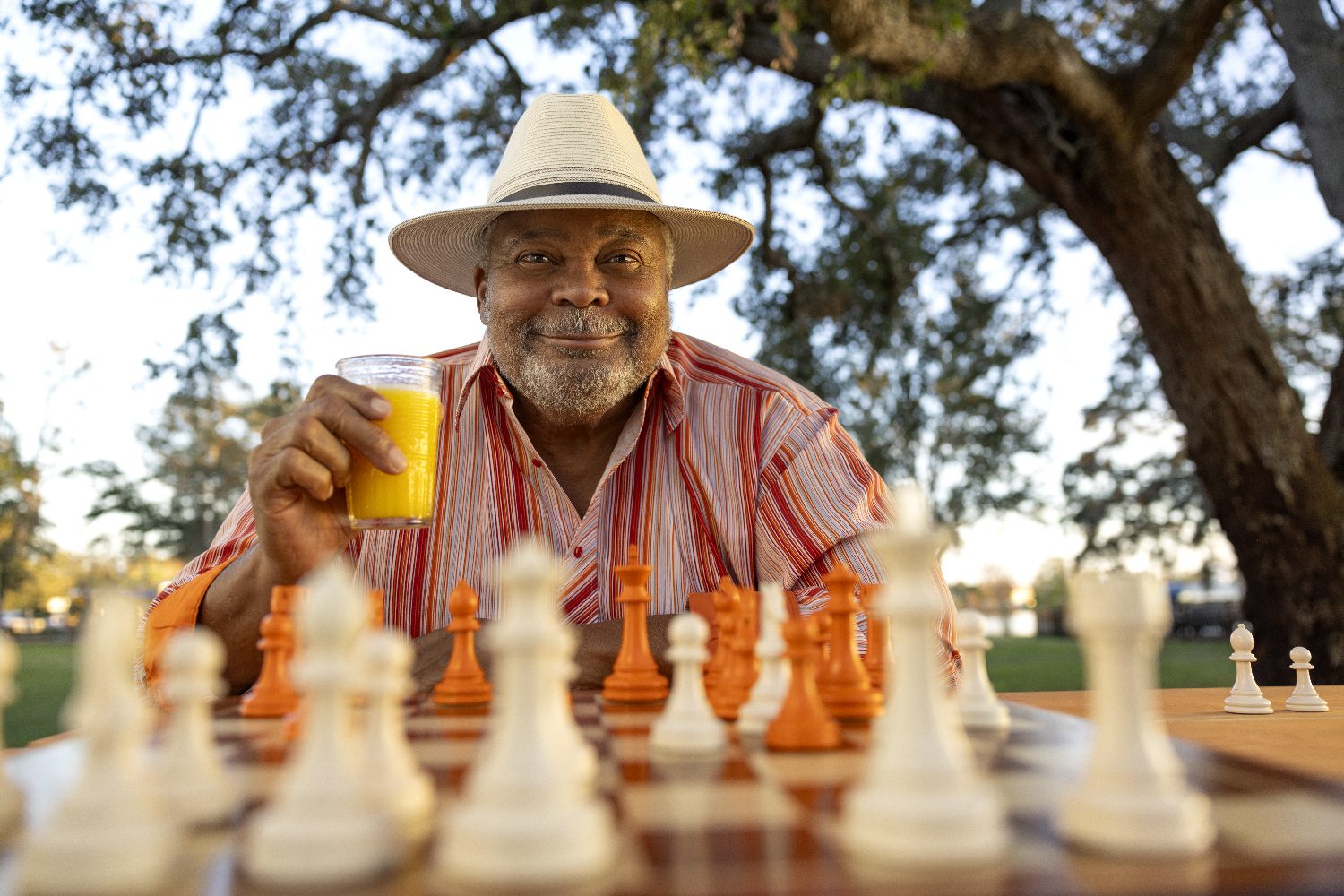 An older man plays chess in the park with orange juice