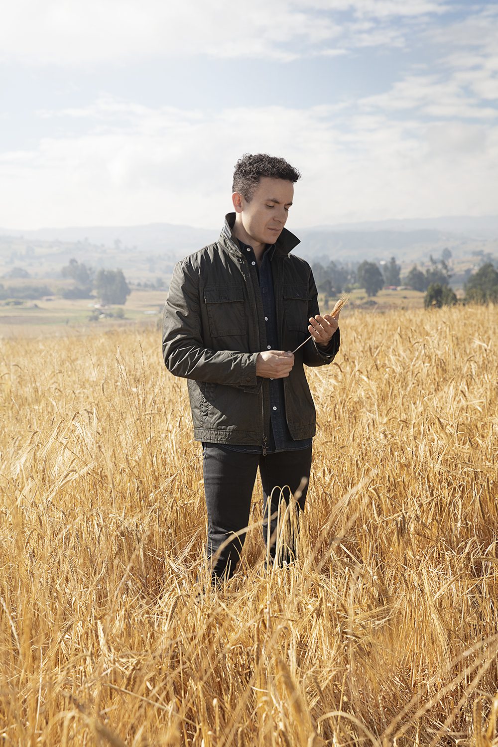 The artist stands full-length in a golden barley field
