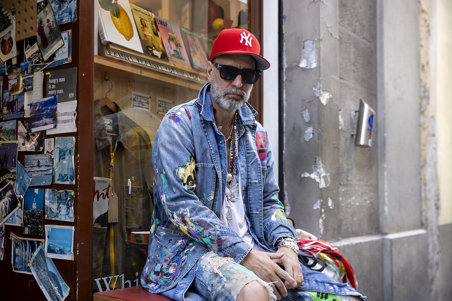 Furia sits outside a Florence shop in a red New York cap and a denim jacket he painted himself